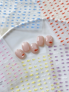 Macro shot of cute cartoon fish nail art stickers on a soft pink false nail