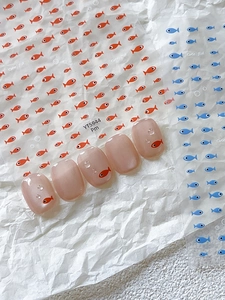Detail of cute mini fish nail stickers with blue and orange patterns on clear nail tips
