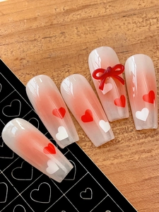 Detail of coral red gradient press-on nails with 3D bows and white heart patterns
