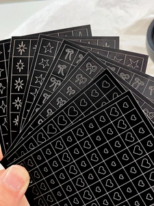 Detailed view of black airbrush nail art stickers featuring gold heart and star patterns