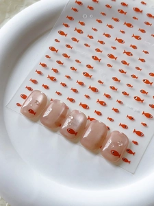 Detail of cute orange fish nail art stickers with 3D water drop effect on nude cat-eye nails