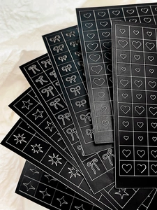 Detail of black nail art stickers featuring white bows, stars and hearts patterns