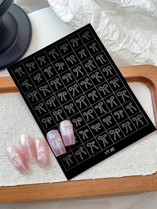 Detail of silver bow nail stickers applied on pink gradient nails with pearl accents