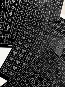 Close-up of black nail stickers with white heart, star and bow patterns on grid sheets