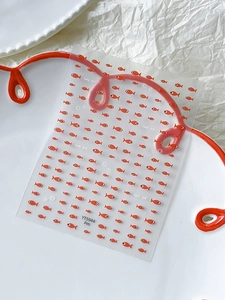Detail of cute orange fish nail art stickers on a white ceramic plate for DIY decoration