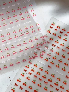 Macro di adesivi per unghie semitrasparenti con motivi di ciliegie e fiocchi su sfondo pietra