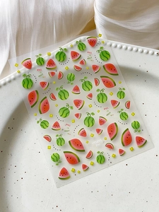 Close-up of cute watermelon nail art stickers and yellow flowers on a white ceramic tray