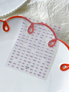 Macro shot of purple cartoon fish nail art stickers on a white plate with wavy red edge