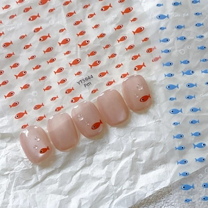 Cute fish nail stickers on pink nails with blue and orange cartoon designs on white paper