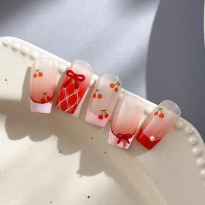 Unghie finte con ciliegie, fiocchi rossi, motivi a rombi e perle su vassoio decorativo