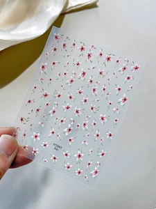 Close-up of translucent floral nail art sticker with red white petals and green leaves
