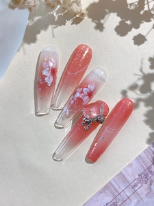 Detail of coral pink gradient coffin nails with cherry blossom art and 3D bow jewelry