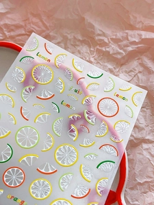Macro detail of embossed 3D lemon and orange fruit nail art stickers on a pink background