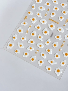 Macro shot of 3D embossed fried egg nail stickers with cute white and yellow patterns