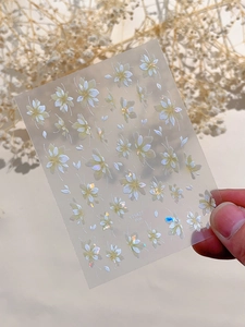Detailed macro shot of white floral nail art stickers with subtle golden shimmer glitters