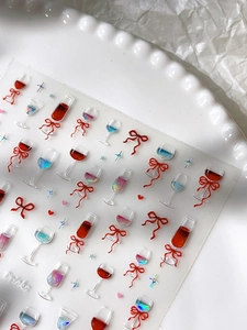 Close-up of 3D embossed nail art stickers featuring wine glasses and red bows