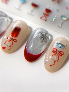 Detail view of nail stickers with red wine glass patterns and 3D bow tie decorations