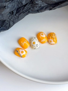 Detail of yellow egg themed press-on nails with bow lines and 3D silver fork charm