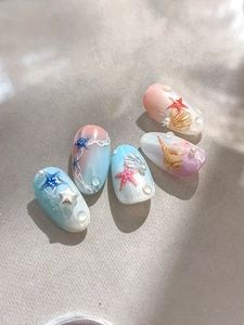 Macro shot of 3D starfish and gold shell charms on gradient ocean themed press-on nails