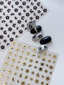 Detailed view of floral nail stickers with black and gold five-petal flowers and rhinestones