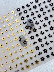 Close-up of black and gold five-petal flower nail decals with glitter rhinestone accents