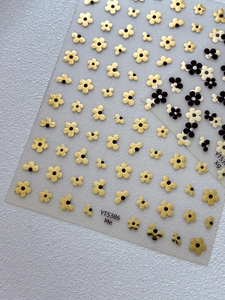 Detailed close-up of self-adhesive five-petal flower nail art stickers in gold and black