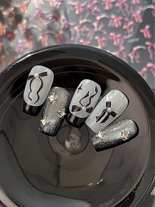 Détail d'ongles faits main avec nœuds noirs, perles blanches et cristaux étincelants