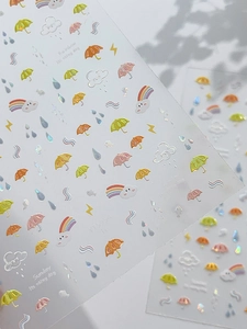 Macro detail of rainbow raindrop nail stickers with laser glitter finish and clouds