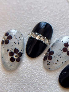 Macro shot of oval press-on nails with black floral patterns and horizontal rhinestones