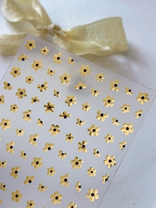 Close-up of golden five-petal flower nail art stickers with black center details
