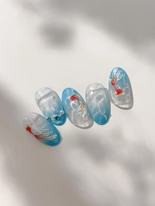 Macro detail of oval press-on nails featuring gradient blue base and hand-painted goldfish