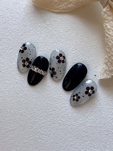 Detail of oval press-on nails with black five-petal flowers and silver rhinestones