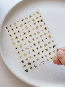 Detail view of golden five-petal flower nail stickers with metallic gloss on a white plate