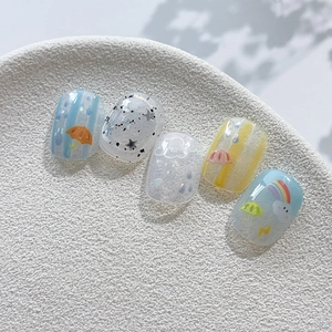 Macaron press-on nails set with rainbow and cloud designs on a ceramic tray