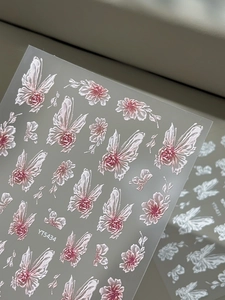 Detailed macro view of 3D embossed nail stickers with pink roses and white butterfly wings