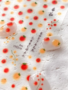 Macro detail of tomato nail art stickers on clear tips with red and orange fruit patterns