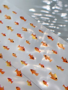 Macro shot of 3D orange fish nail art stickers with metallic finish and water ripples