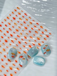 Detail of cute orange fish nail art stickers applied on sparkling blue manicure tips