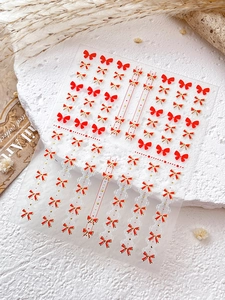 Détail macro de stickers pour ongles nœuds rouge et or sur une surface en pierre