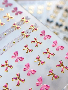 Détail macro de stickers ongles 3D avec nœuds dégradés roses et bords dorés gaufrés