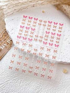 Détail d'autocollants pour ongles nœud rose avec bords dorés et motifs de dentelle