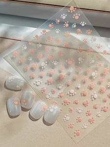 Detail of pink and white cat paw nail stickers on transparent backing with grey sample tips