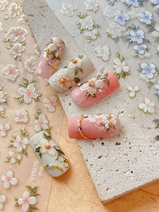 Macro detail of 3D embossed floral nail stickers with gold leaf accents on pastel nails