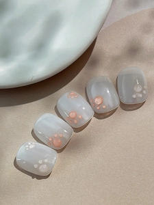 Close-up of 3D pink cat paw nail charms on translucent milky white press-on nails