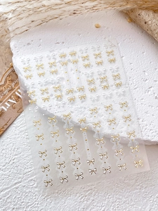 Vue détaillée des autocollants pour ongles avec nœuds blancs et dorés sur une surface texturée