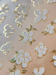 Detailed macro view of white floral nail art stickers with embossed gold metallic edges