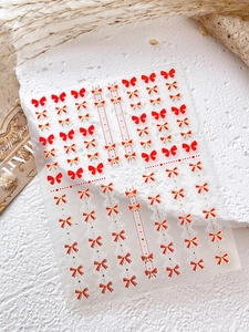 Détail de stickers à ongles nœud rouge avec accents dorés sur surface en pierre blanche