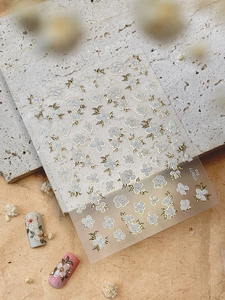 Detail of white and blue flower nail stickers with gold edges on stone background