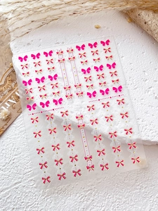 Détail d'autocollants pour ongles à nœuds roses et dorés sur un support en pierre
