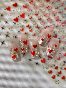 Detailed view of gold star and red heart nail art stickers applied on pink manicure